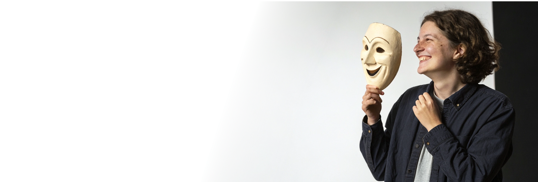 Улыбающийся человек держит театральную маску символ анонимного обращения к психологу